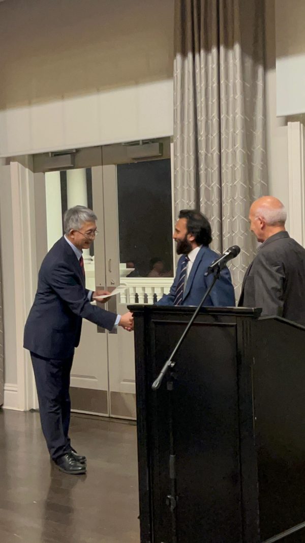 Sharoon shaking hands and receiving a certificate at a podium during an award ceremony