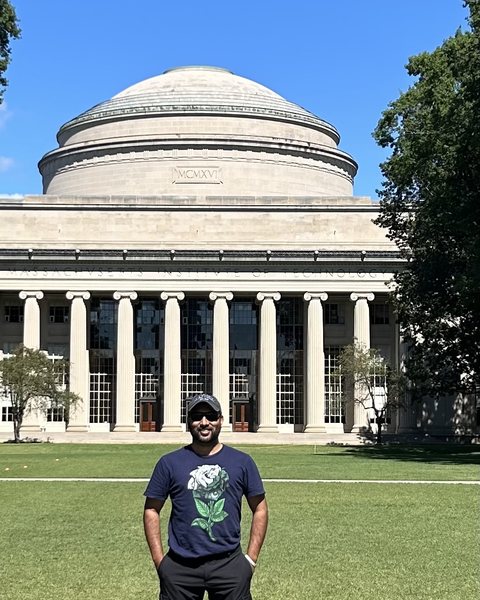 Sharoon Sharif standing on a lawn in front of a domed, columned building on a sunny day